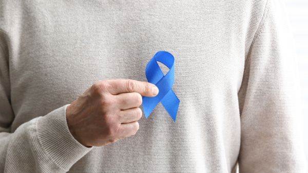 Idoso segurando fita azul relacionada ao Março Azul, campanha que promove importância de rastreamento de câncer colorretal
