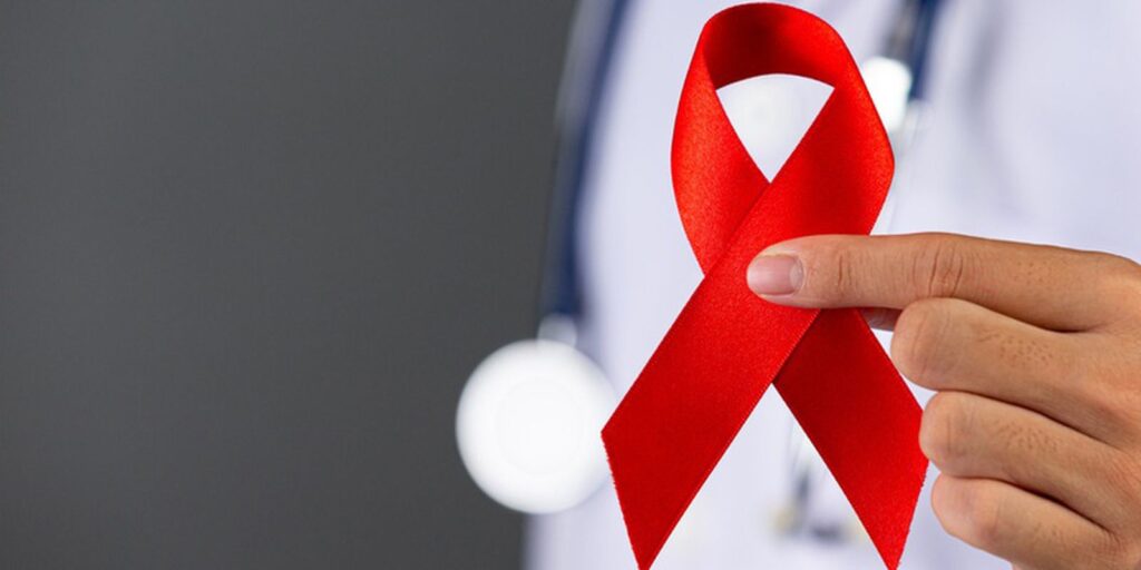 Profissional da saúde segurando fita vermelha, que representa o Dezembro Vermelho, mês da conscientização de pessoas vivendo com HIV / Aids