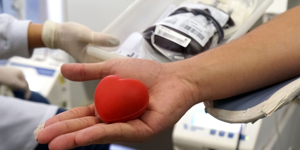 Mão de pessoa com coração vermelho em miniatura representando doação de sangue em local de coleta
