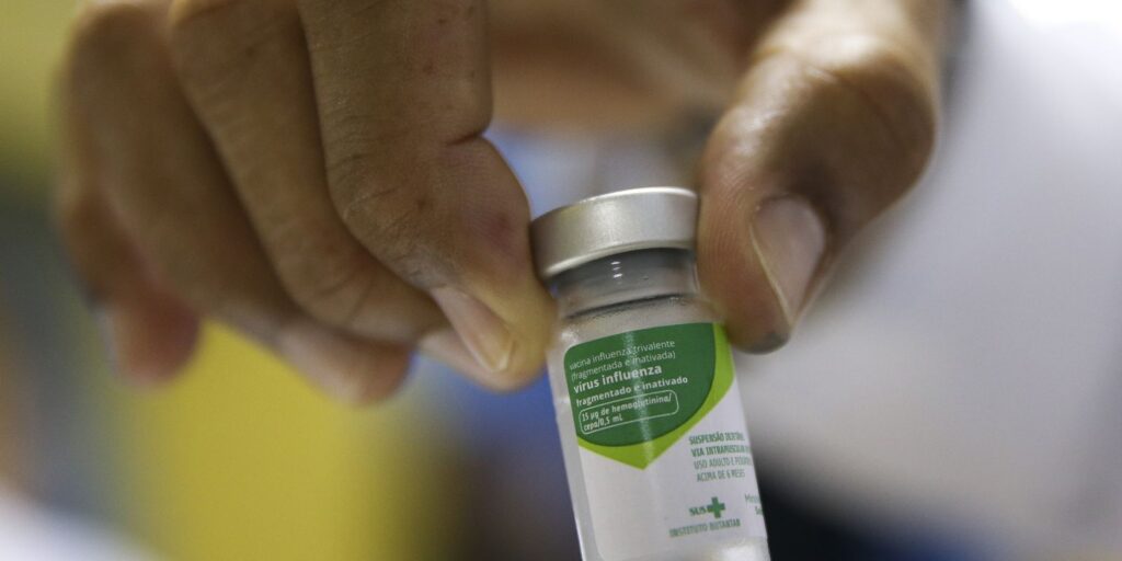 Profissional de saúde segurando frasco com agentes conta vírus da gripe antes de aplicar vacina em paciente