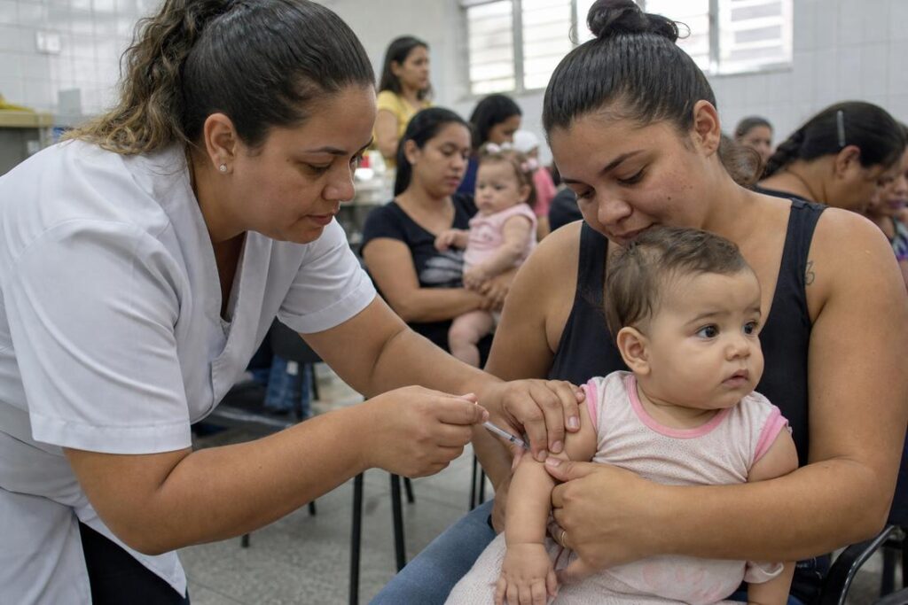 Profissional de saúde aplica vacina tríplice viral em criança durante campanha contra o sarampo em São Paulo.