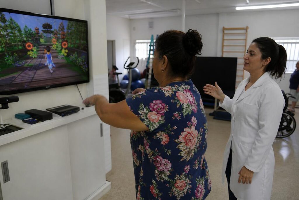 Paciente usa videogame na reabilitação com apoio de fisioterapeuta em São Vicente