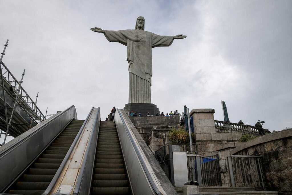 Escadas rolantes de acesso ao Cristo Redentor com a estátua ao fundo e andaimes de obras à esquerda, sob céu nublado